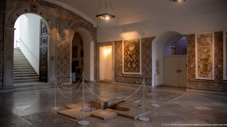 Museum room with tall Christian inscription mosaics, patterned walls, stairs, arches, and roped-off floor fragments.