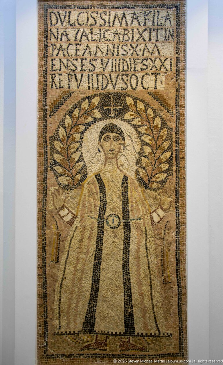 Frontal woman in a tall Christian funerary mosaic beneath a Latin inscription and leafy arch or wreath.