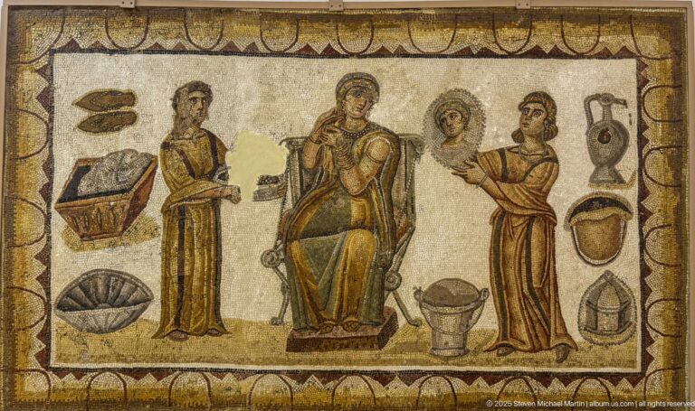 Seated woman with two female attendants, mirror, vessels, box, basin, and grooming objects in a Roman mosaic.