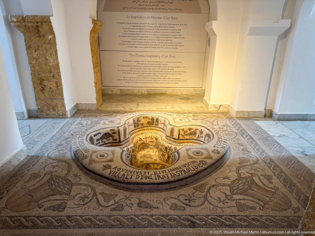 Bardo Museum display of the Demna baptistery with four-lobed mosaic font, surrounding pavement, inscriptions, and Christian symbols.
