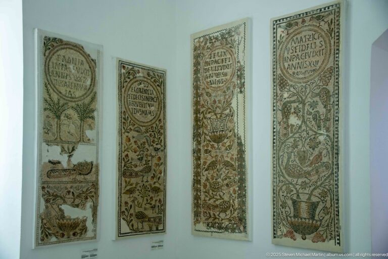 Four tall Christian mosaics with Latin inscriptions, vases, birds, trees, vines, and floral motifs displayed together.