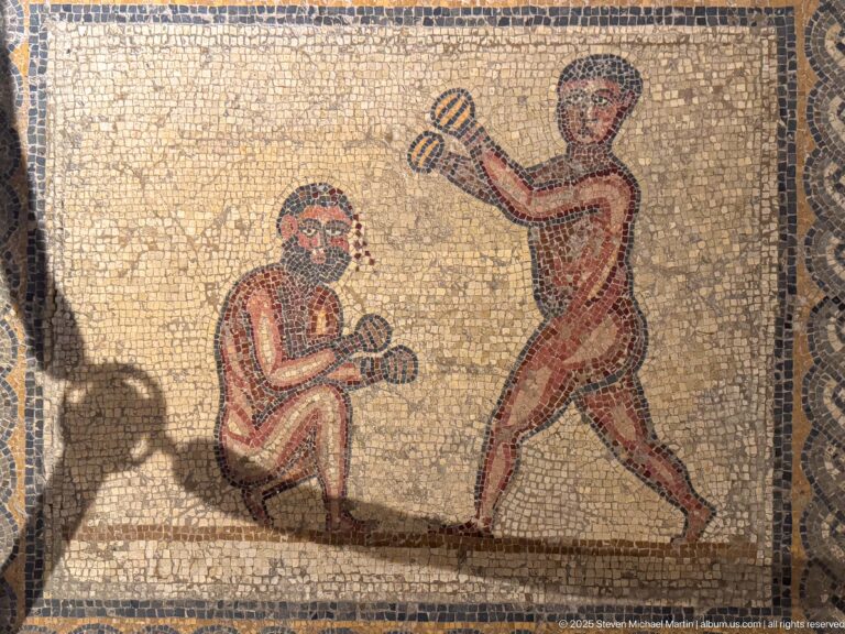 Two nude Roman boxers with wrapped fists, one crouching defensively while the other advances to strike.