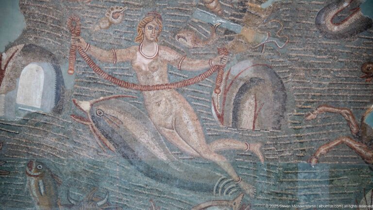 Semi-nude female figure in a Roman marine mosaic surrounded by large fish and curling sea creatures.