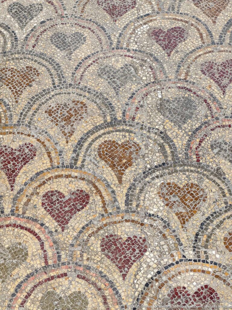 Close view of overlapping mosaic scallops outlined in dark tesserae with red, ochre, and gray heart-shaped centers.