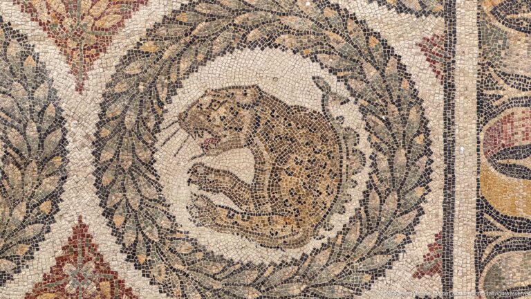 Spotted feline curled inside a leafy circular wreath in a Roman animal mosaic.