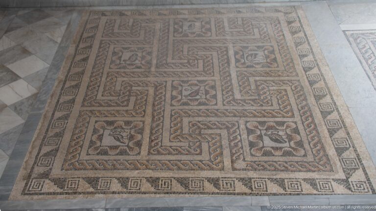 Rectangular geometric mosaic with interlocking meanders, floral compartments, corner motifs, and Greek-key outer border.
