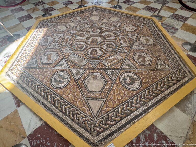 Oblique view of a square Roman mosaic with polygonal portrait and animal panels, circular medallions, and braided border.