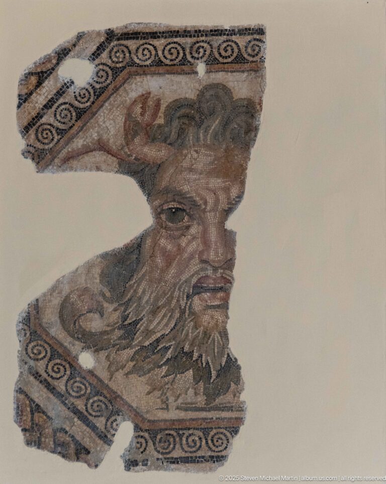 Fragmentary mosaic head of a bearded man with horn-like attributes, curling dark hair, and surviving meander borders.
