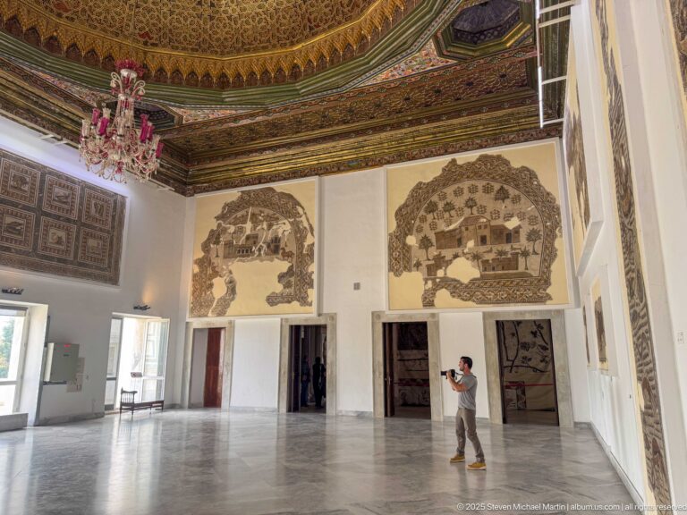 Visitor in an ornate Bardo Museum gallery beneath two large fragmentary landscape mosaics and a richly decorated ceiling.
