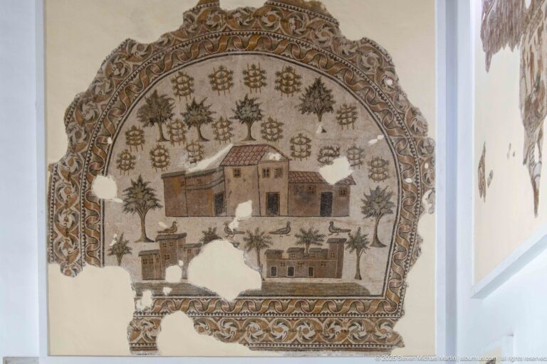 Arched Roman landscape mosaic with central villa, rows of trees, smaller buildings, ornate border, and areas of loss.