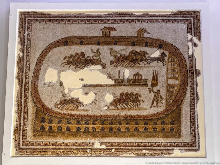 Roman circus mosaic with quadriga teams racing around a central spina and a standing figure at the right edge.