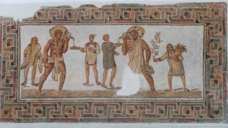 Six standing men carrying staffs, vessels, and a basket-like load inside a bold geometric mosaic border.