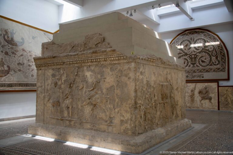 Close view of a large stone monument with worn figural relief carving and projecting moldings.