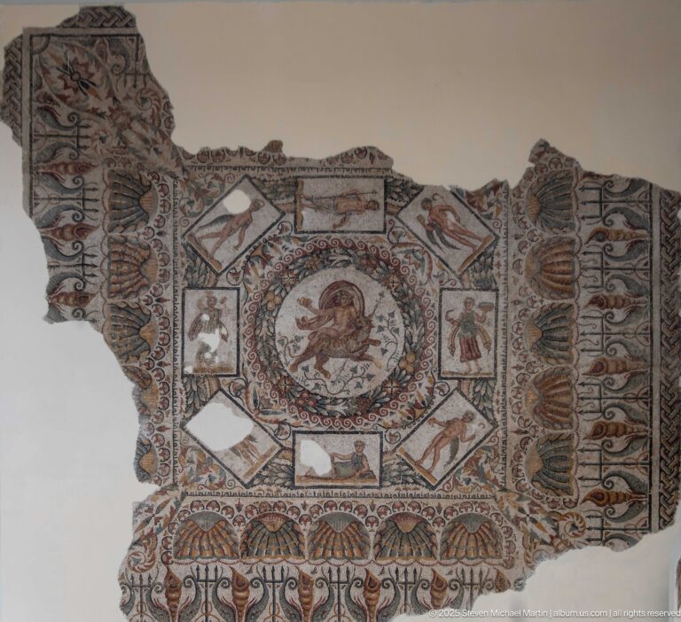 Fragmentary Roman mosaic with central horseman medallion, smaller figural panels, and dense floral-geometric borders.
