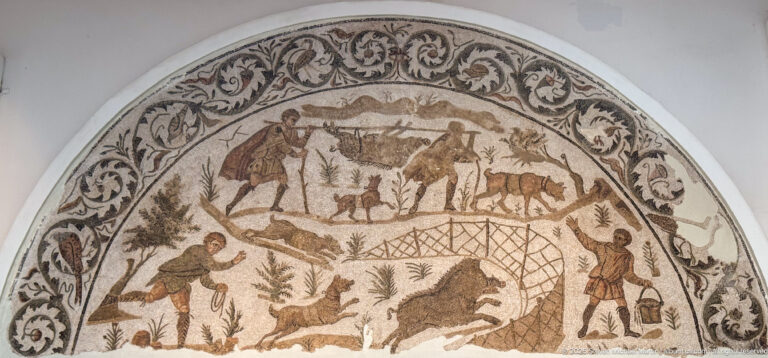 Semicircular Roman mosaic with hunters, dogs, wild game, and a large net used to trap animals in a landscape.