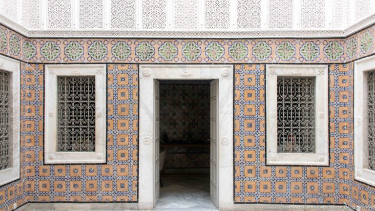 Polychrome tiled courtyard wall with central doorway, two iron-grilled windows, and decorative friezes at Dar Jeld Hotel.