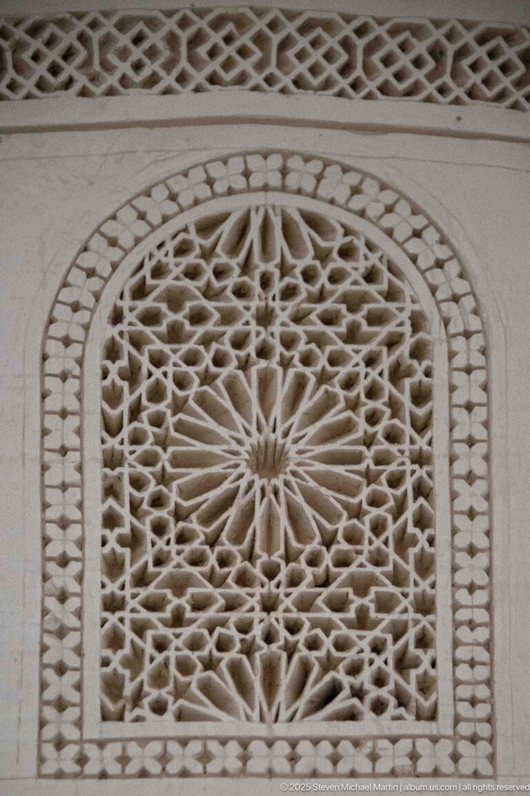 Arched pierced plaster grille with radial star pattern and dense geometric openwork, beneath a second lattice band.