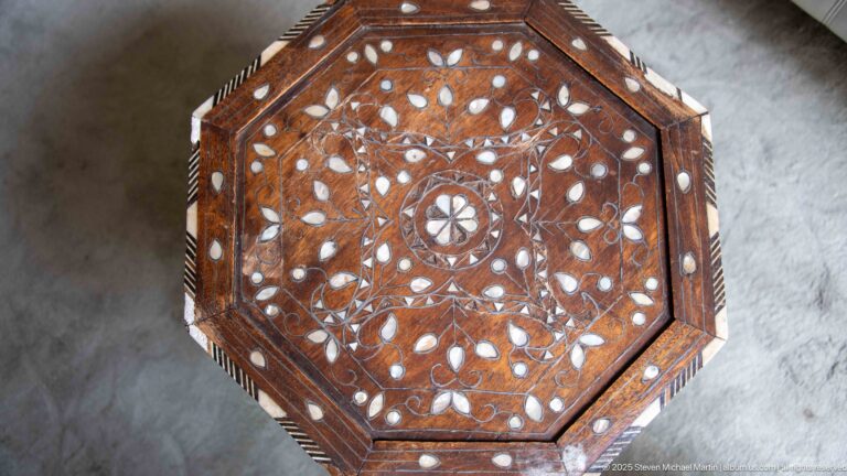 Top-down view of octagonal wooden table with dense geometric inlay, pale inserts, central rosette, and worn edges.