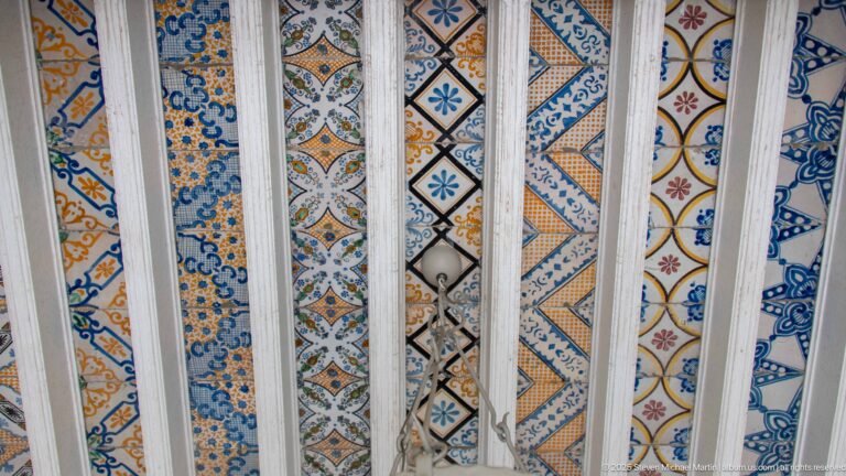 Close view of blue, ochre, red, and black patterned tiles seen through evenly spaced white grille bars.