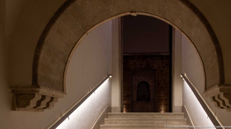 Large stone arch frames marble stairs with illuminated handrails leading to a carved recessed niche at the landing.