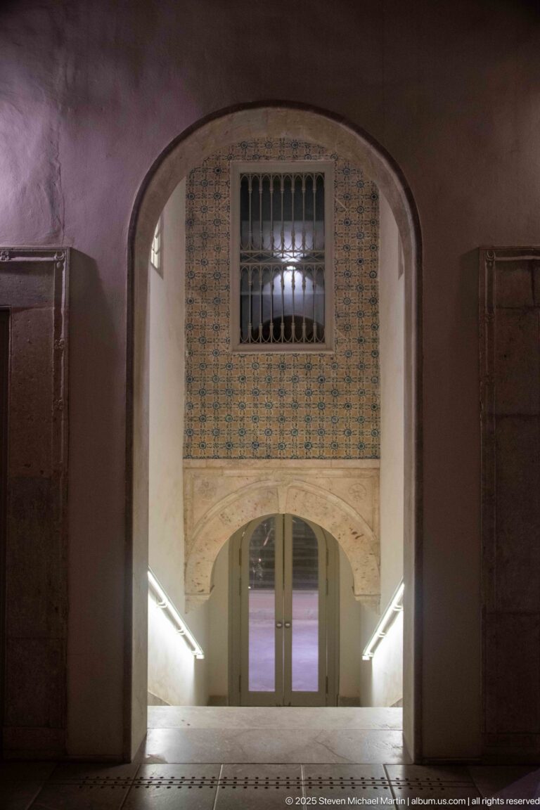 Stair landing with patterned tile wall, barred window, carved lower arch, and bright handrail lighting.