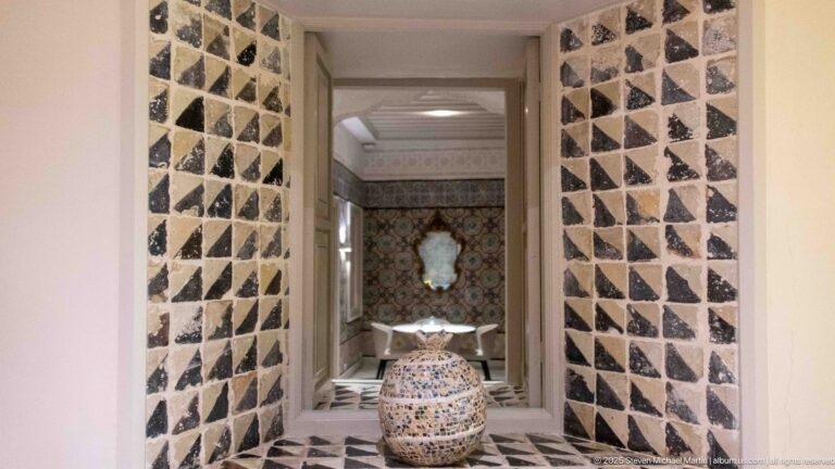 Large patterned ceramic jar before a mirror, surrounded by black-and-light triangular wall inlay and colorful tilework beyond.