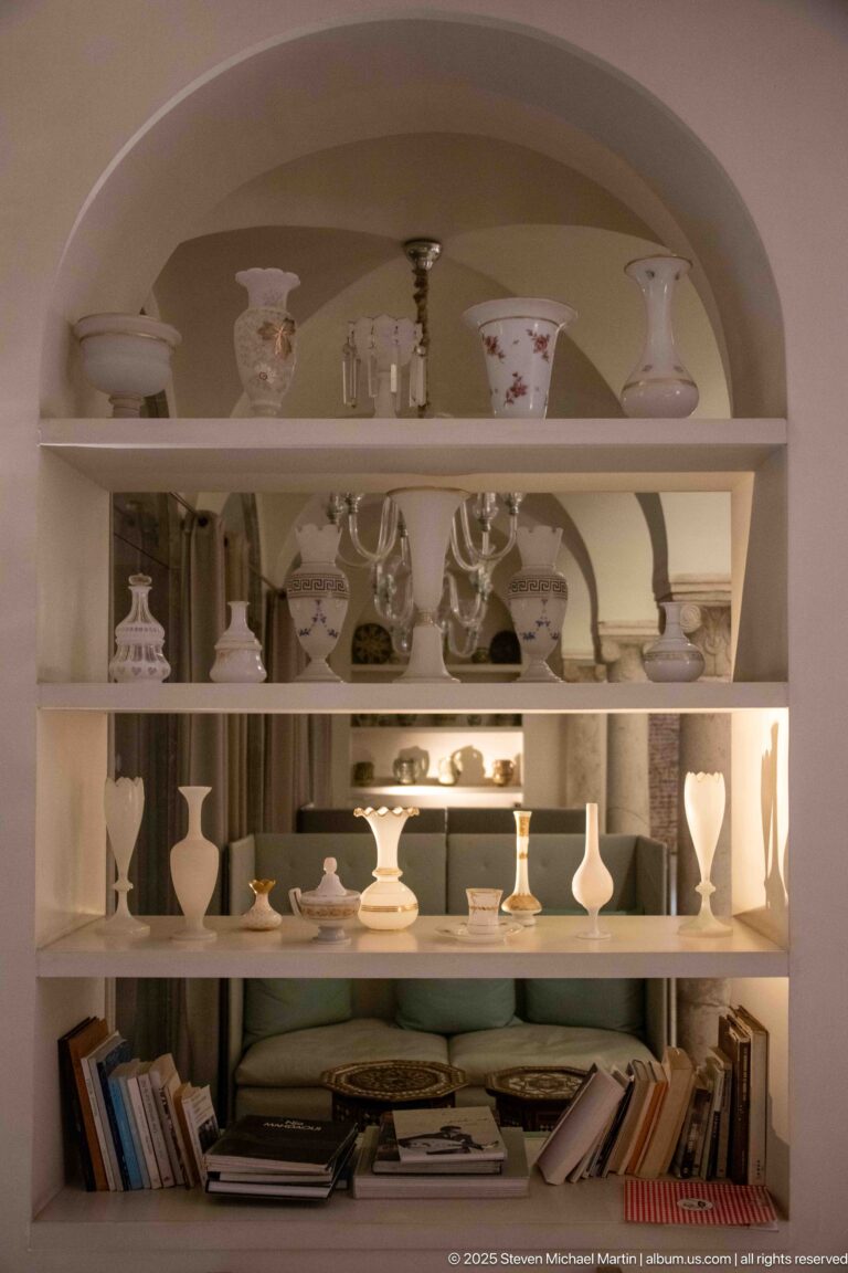 Arched built-in shelving filled with white and patterned ceramics, decorative objects, and books on the lower shelf.