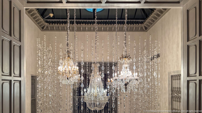 Several illuminated crystal chandeliers hang amid long vertical strands of glass drops in a tall interior space.