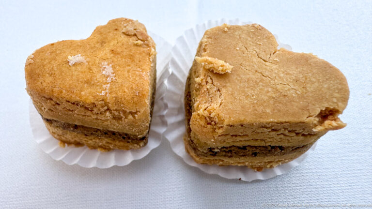 Two small heart-shaped golden pastries with visible layered interiors resting on white paper cups against a white cloth.