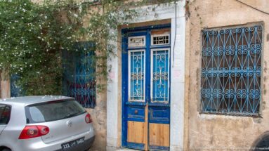 Blue-framed double door with wood lower panels and decorative iron grilles beside a matching blue barred window.