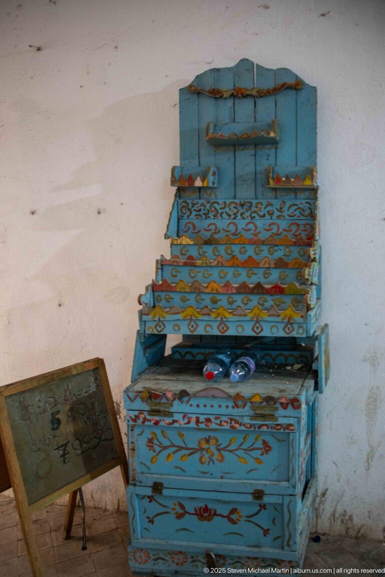 Blue stepped wooden chest with hinged compartments, painted floral and geometric motifs, and worn surfaces against a plain wall.