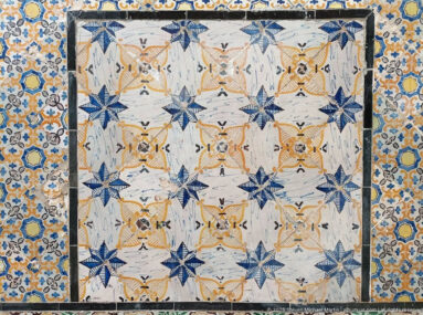 Rectangular ceramic panel with repeated blue star motifs, ochre rosettes, pale geometric forms, and a dense floral border.