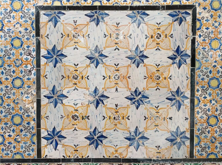 Rectangular ceramic panel with repeated blue star motifs, ochre rosettes, pale geometric forms, and a dense floral border.