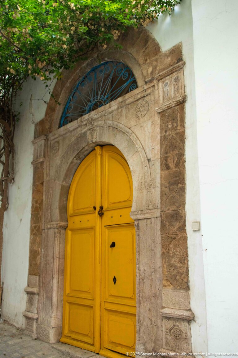 Yellow arched double door in a carved stone surround beneath a semicircular blue iron fanlight.