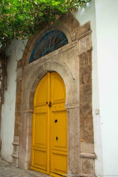 Yellow arched double door in a carved stone surround beneath a semicircular blue iron fanlight.