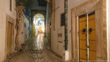 Studded yellow double door with ring knockers beside a narrow cobbled lane receding through arches at night.