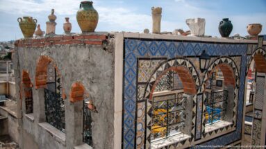 Rooftop wall with red-brick arches, patterned tile borders, black metal grilles, and ceramic vessels displayed along the parapet.