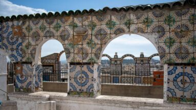 Two rounded rooftop arches covered with multicolored ceramic tiles, opening toward additional tiled railings and the distant roofscape.