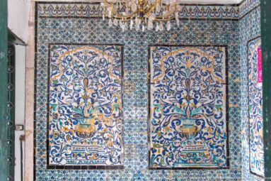Two large blue-and-ochre floral ceramic panels with urn motifs set within a densely patterned tiled interior wall.
