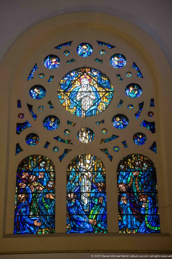 Large blue stained-glass ensemble with three figurative lower panels, central roundel, and many small colored openings.