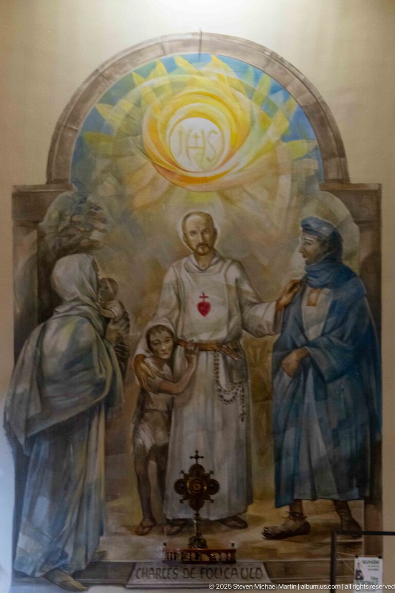 Devotional mural with a haloed cleric bearing a Sacred Heart emblem, two standing figures, and radiant IHS monogram above.