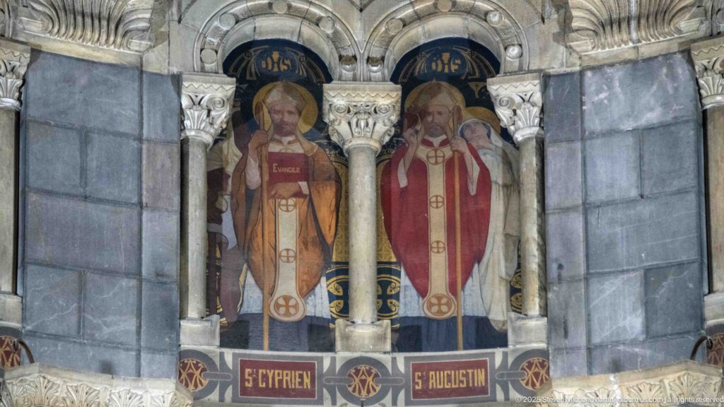 Painted Saint Cyprian and Saint Augustine in episcopal vestments, labeled beneath adjacent arched niches in the cathedral apse.