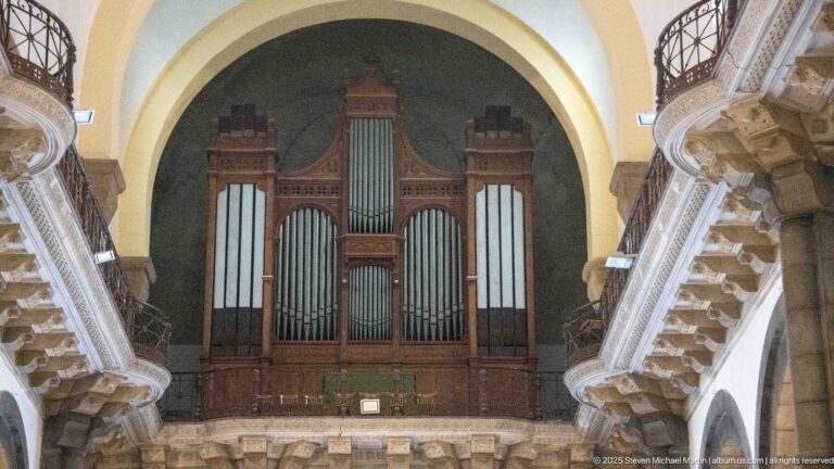 Large wooden pipe organ with multiple ranks of metal pipes filling an arched gallery opening at the rear of the cathedral.