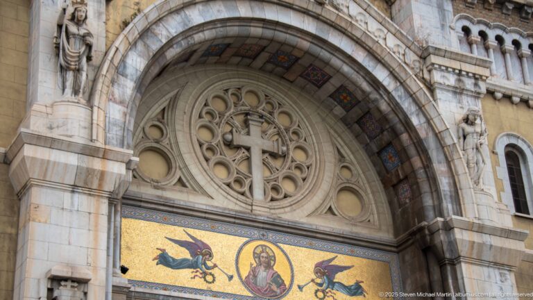 Stone cross and circular tracery above a gold mosaic of Christ with winged figures on the cathedral façade.