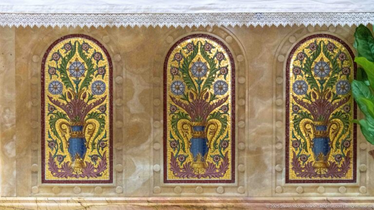 Three arched altar-front panels with stylized flowering plants in blue urns on gold grounds beneath a white lace-edged cloth.