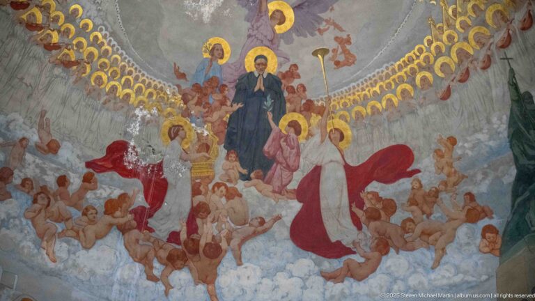 Close view of the apse mural with a central haloed figure, angels, gold halos, and numerous figures across the curved vault.