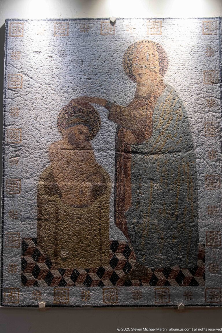 Rectangular mosaic with two haloed standing figures, one extending an arm toward the other, bordered by dark geometric patterning.