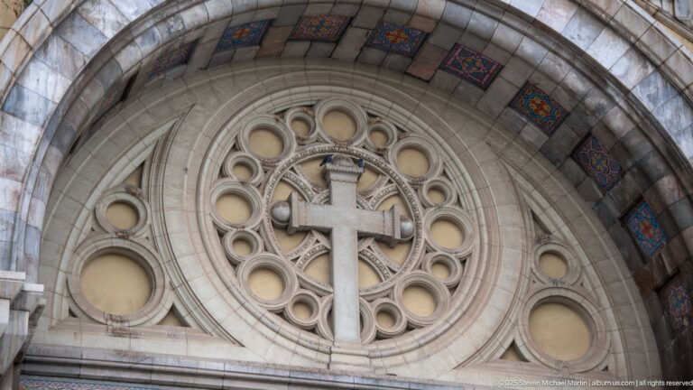 Latin cross centered in circular stone tracery beneath the decorated entrance arch of St. Vincent de Paul Cathedral.
