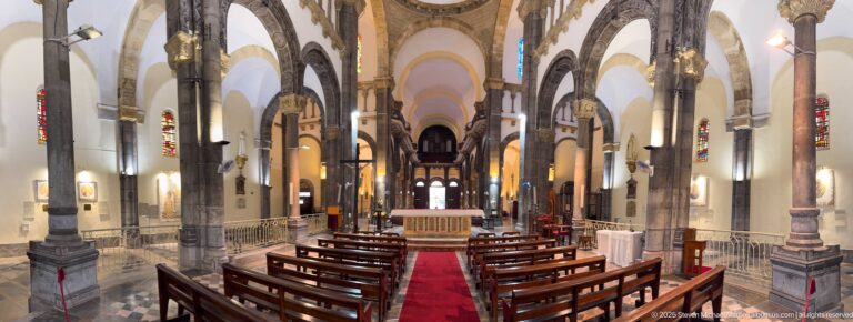 Central aisle with red carpet and wooden pews leading toward the altar beneath tall stone columns and arches.