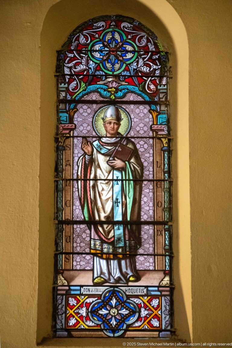 Arched stained-glass window of a haloed cleric labeled “BONIFATIUS,” holding a crozier and raising one hand in blessing.
